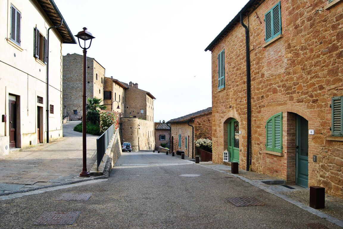 A narrow street lined with stone buildings, some with arched doorways and shutters.