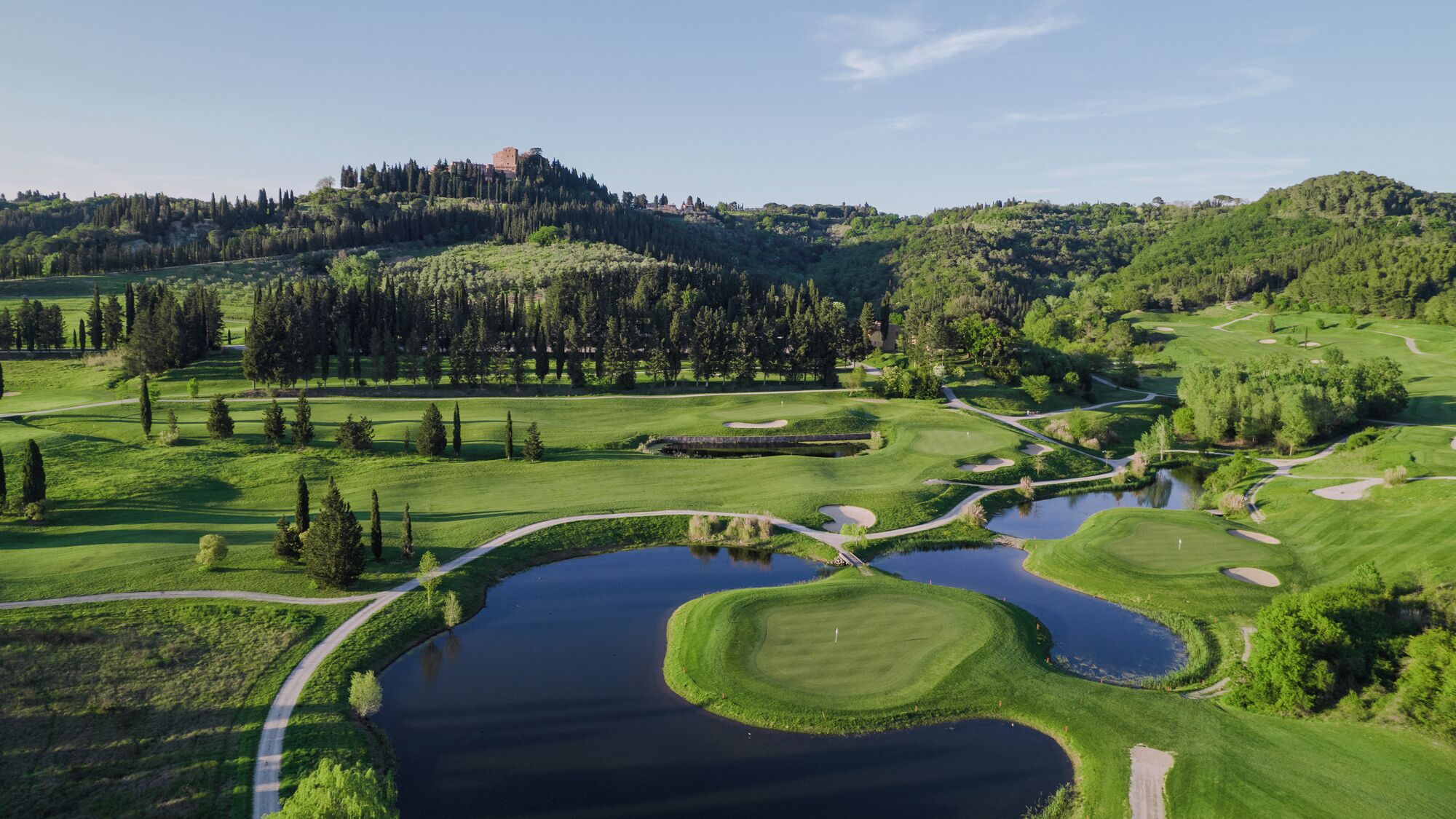 A golf course with ponds, pathways, and a castle on a hill in the background.
