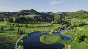 A golf course with ponds, pathways, and a castle on a hill in the background. - Divinely situated in front of the Castle of Castelfalfi, in the heart of Tuscany (Florence)