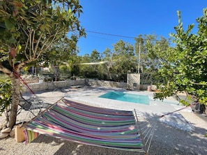 A backyard with a pool, a hammock, and a stone wall.