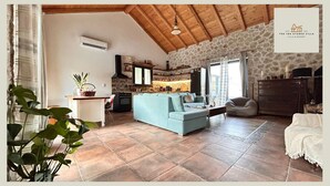 Una sala de estar con sofá, un comedor con mesa y sillas, una cocina con estufa y alacenas, y una pared de piedra.