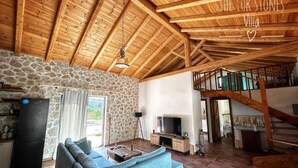 Una sala de estar con pared de piedra, un sofá, un televisor, una escalera y una zona de cocina.