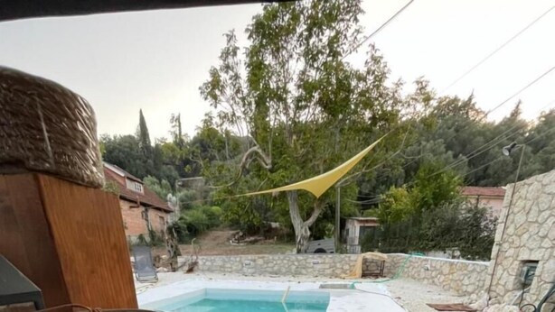 Una estera tejida, una maceta de cerámica y una piscina con toldo amarillo en un patio trasero.