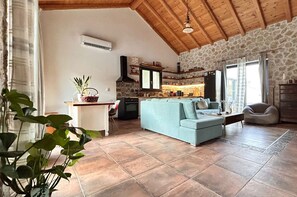 Un salon avec un canapé, un coin repas avec une table et des chaises, une cuisine équipée d’une cuisinière et de placards, et un mur en pierre.