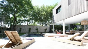 A modern outdoor pool area with wooden loungers and a stone wall.