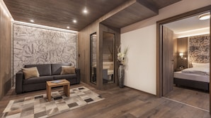 A modern room with a dark brown wooden floor, a grey sofa with cushions, a wooden coffee table, and a large map wallpaper. There is a mirror, a vase with flowers, and a bed with a white headboard. - Fliana Residenz (Ischgl)