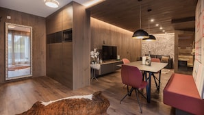 A modern living room with a wooden floor, a dining area with a table and chairs, a sofa, and a TV. - Fliana Residenz (Ischgl)
