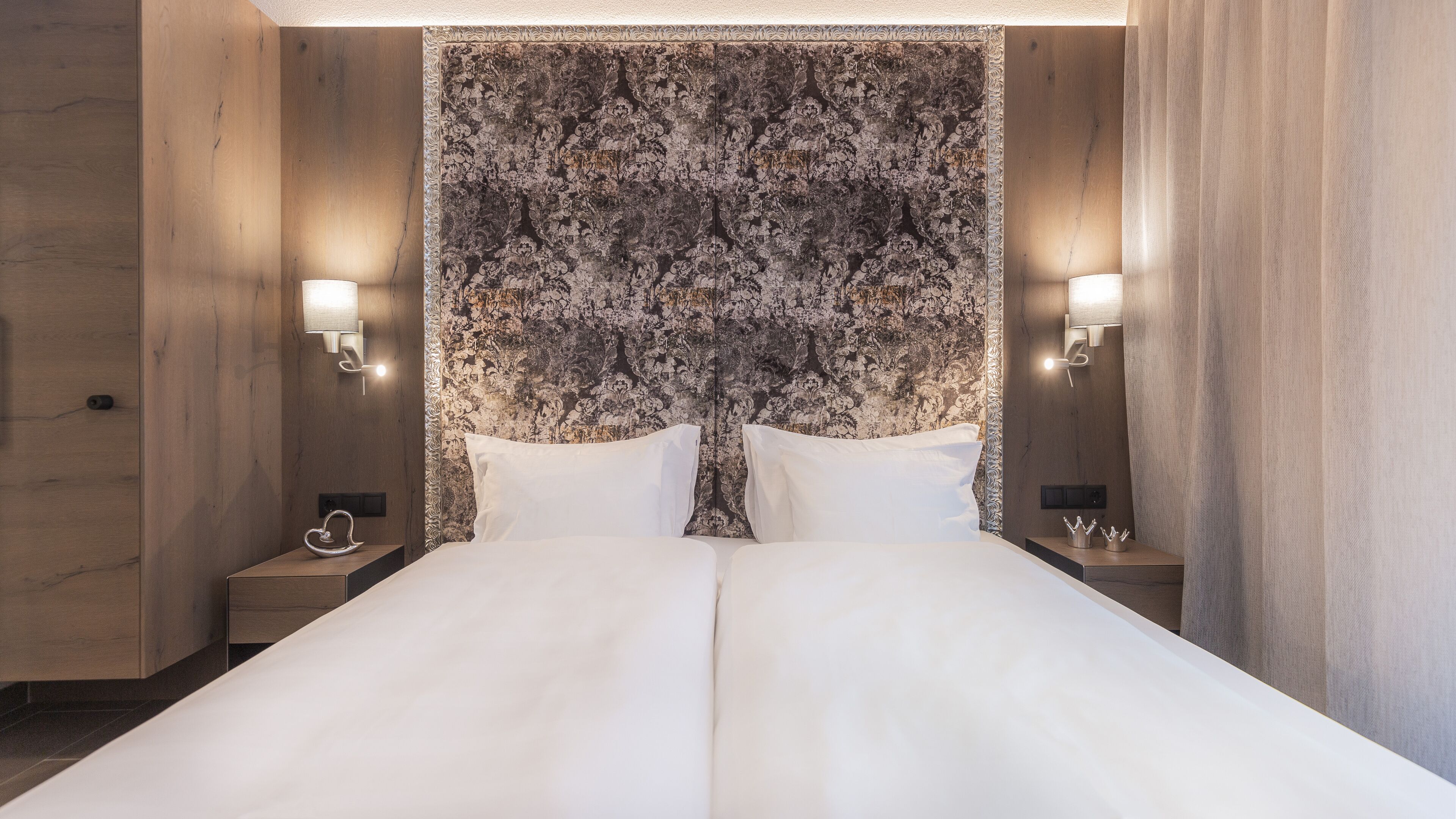 A double bed with white linens, two bedside tables with lamps, and a floral-patterned headboard.