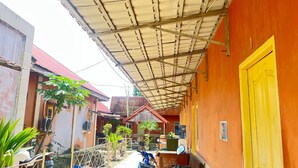 A covered outdoor area with a metal roof, a yellow door, and a red-roofed building in the background. - Hotel O Guest House Leo Patra (Koealabadak)