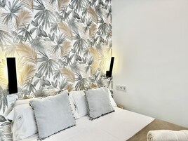 Een slaapkamer met behang met tropische bladeren, een bed met wit bedlinnen en twee bedlampen.