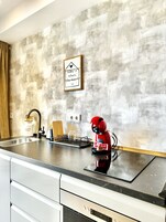 Een moderne keuken met een achterwand van beton, een rood apparaat en een ingelijst citaat aan de muur.