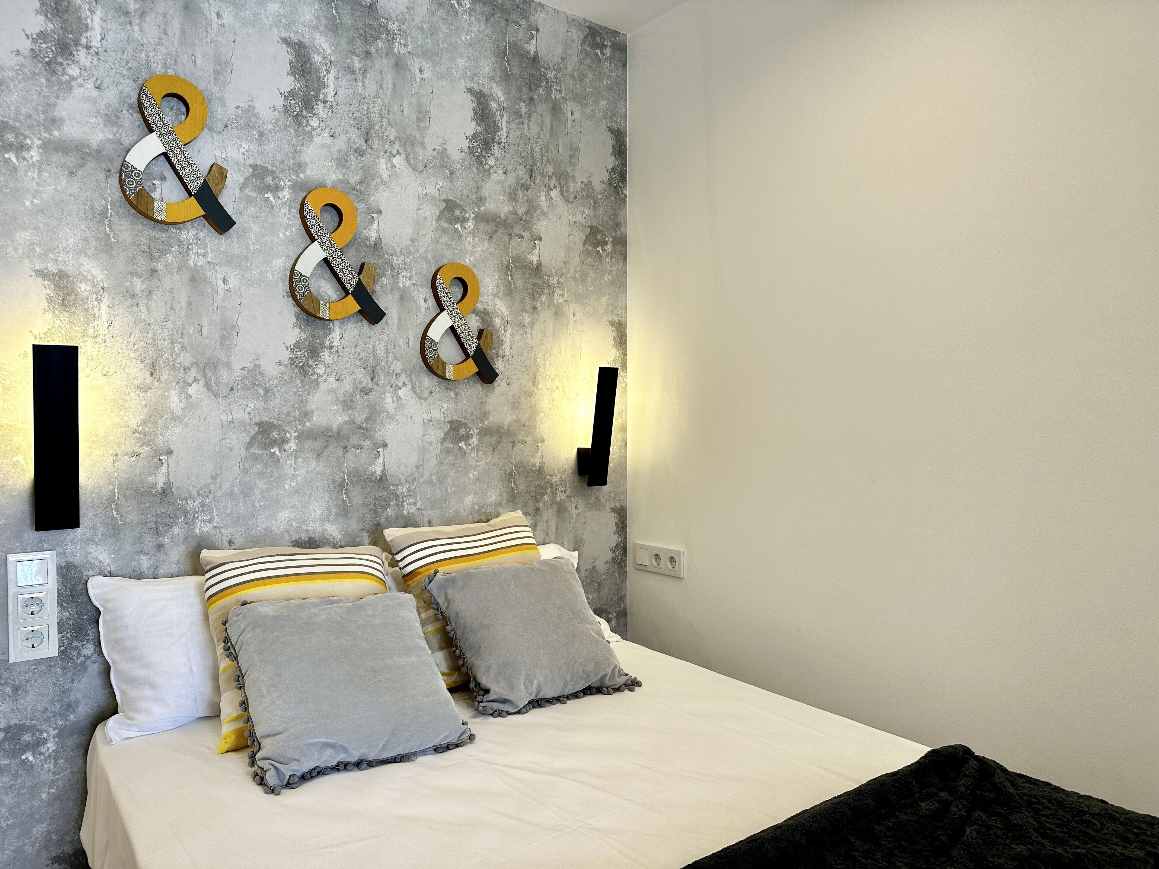 A bedroom with a bed, pillows, and a textured wall with decorative elements.