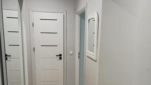 A hallway with wooden flooring, white walls, and a door with horizontal lines. - Apartament Promenada (Rzeszów)