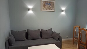 A living room with a grey sofa, a white coffee table, and a wooden chair. There are two wall-mounted lights and a framed picture on the wall. - Apartament Promenada (Rzeszów)
