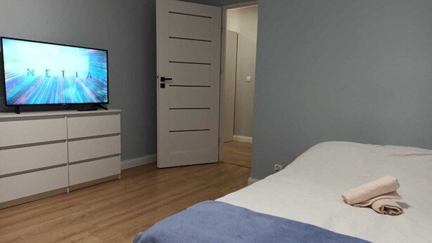A bedroom with a bed, a TV on a dresser, and a door leading to another room. - Apartament Promenada (Rzeszów)