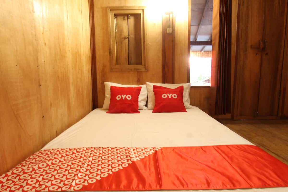 A wooden room with a bed, two red pillows with "OYO" text, a window, and a door.