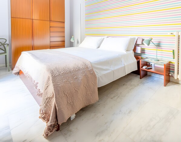 Un lit bien fait, recouvert d’une couvre-lit à motifs floraux, une table de chevet avec une lampe, et un mur à rayures en arrière-plan.