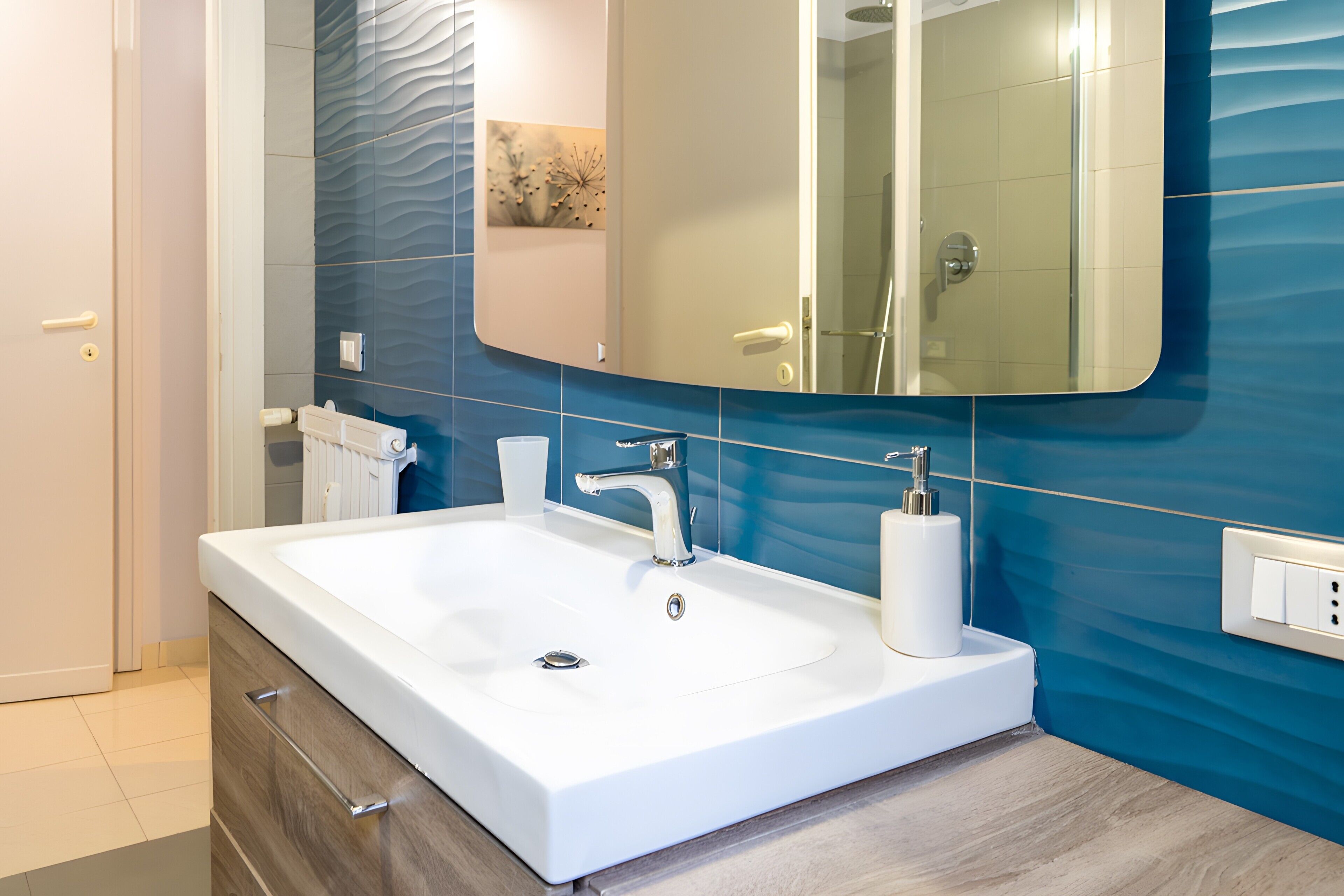 A modern bathroom with a white sink, a large mirror, and blue wall tiles.