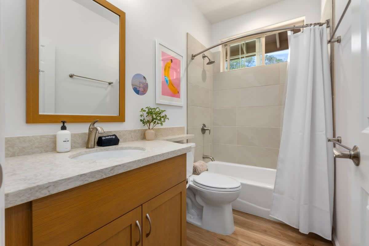 Un baño con tocador de madera, un espejo grande, inodoro, bañera y cortina de ducha.