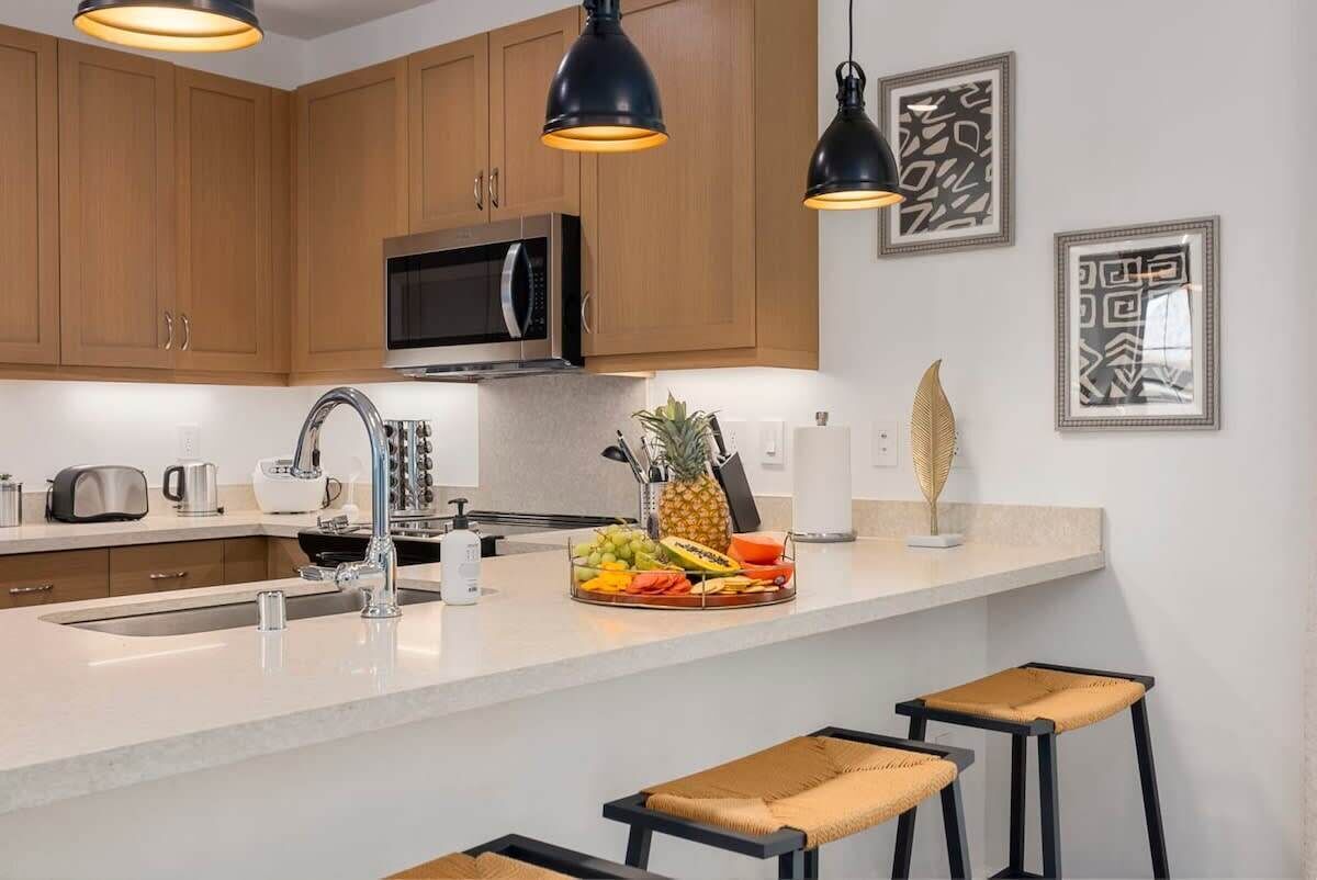 Une cuisine moderne avec des meubles en bois, un four à micro-ondes en acier inoxydable, un évier et deux tabourets de bar.
