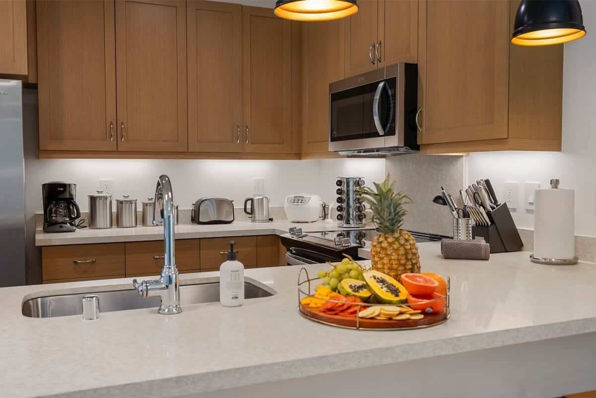 A modern kitchen with wooden cabinets, stainless steel appliances, and a fruit platter on the counter.