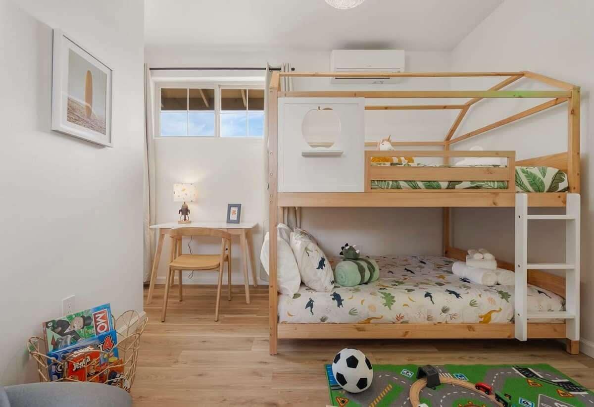A bunk bed with a desk and chair, a window, and a toy soccer ball on the floor.