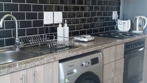Ett modernt kök med träskåp, svart kakel som stänkskydd, rostfria vitvaror samt en inbyggd tvättmaskin och torktumlare.