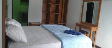 A neatly made bed with a white and blue bedspread, a wooden nightstand, a mirror, and a green door in the background.