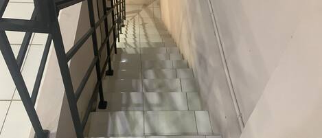 A staircase with a metal railing, tiled steps, and a plain wall.