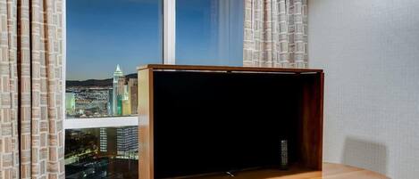 A room with a large window offering a city view, a wooden table, and a remote control on the table.