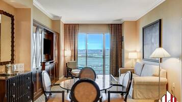 A hotel room with a dining area, a sofa, a TV, and a large window with a view.
