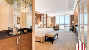 Habitación de hotel con una cama grande, zona de comedor, kitchenette y vistas a la ciudad.