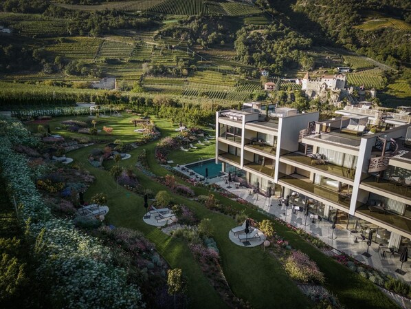 Un hôtel moderne à plusieurs étages, doté d’une piscine sur le toit, entouré de jardins aménagés et de vignobles.