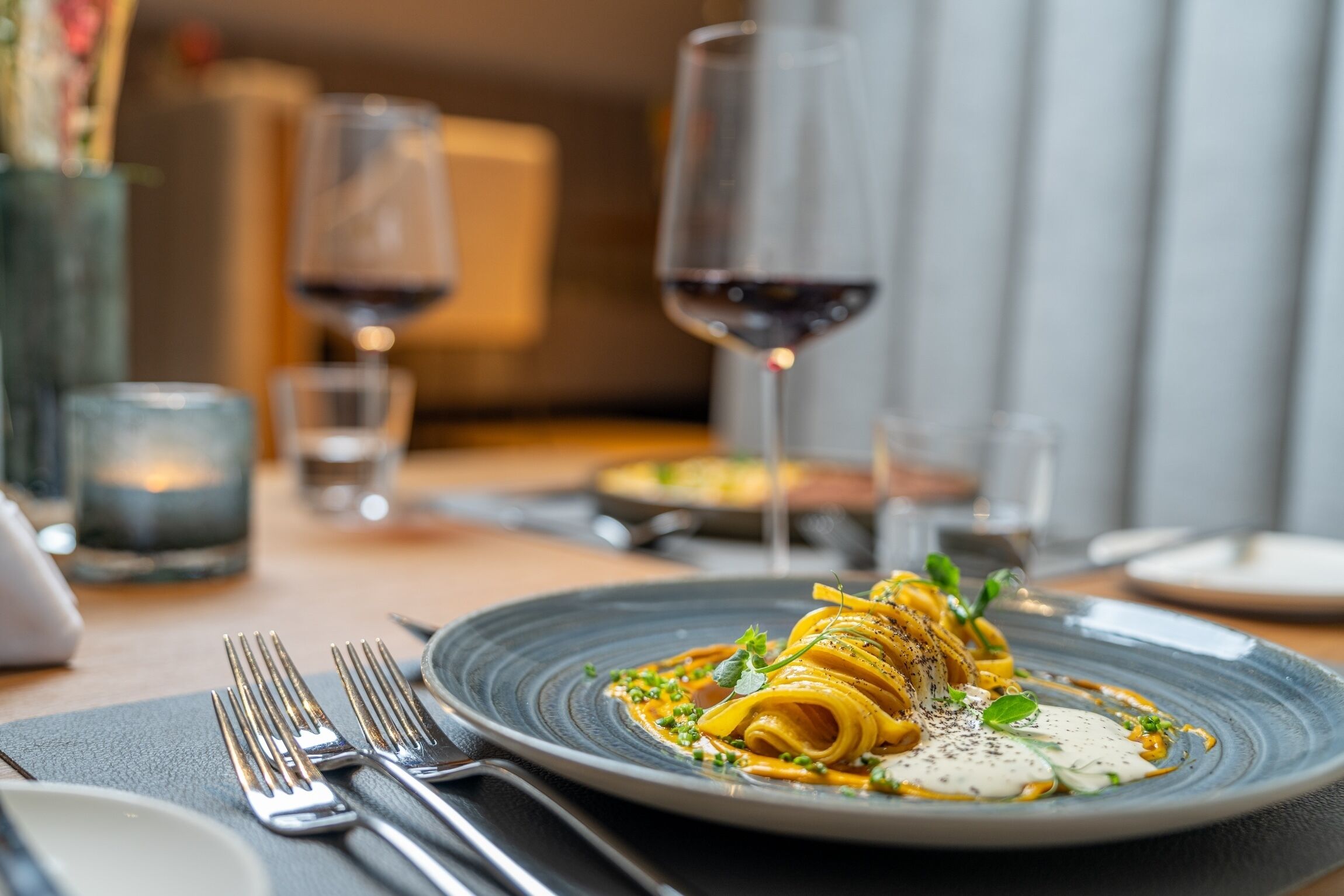 A dining table with a plate of pasta, wine glasses, and cutlery.