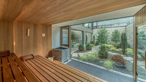 A modern interior with wooden paneling, a stone wall, and a view of a landscaped garden through large windows. - Boutique Hotel Amaril (Castelbello-Ciardes)