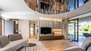 A modern living room with a curved ceiling, a flat-screen TV, and a large window overlooking a garden. - Boutique Hotel Amaril (Castelbello-Ciardes)