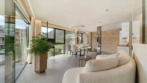 A modern living room with a large window, a sofa, a dining area, and a potted plant. - Boutique Hotel Amaril (Castelbello-Ciardes)