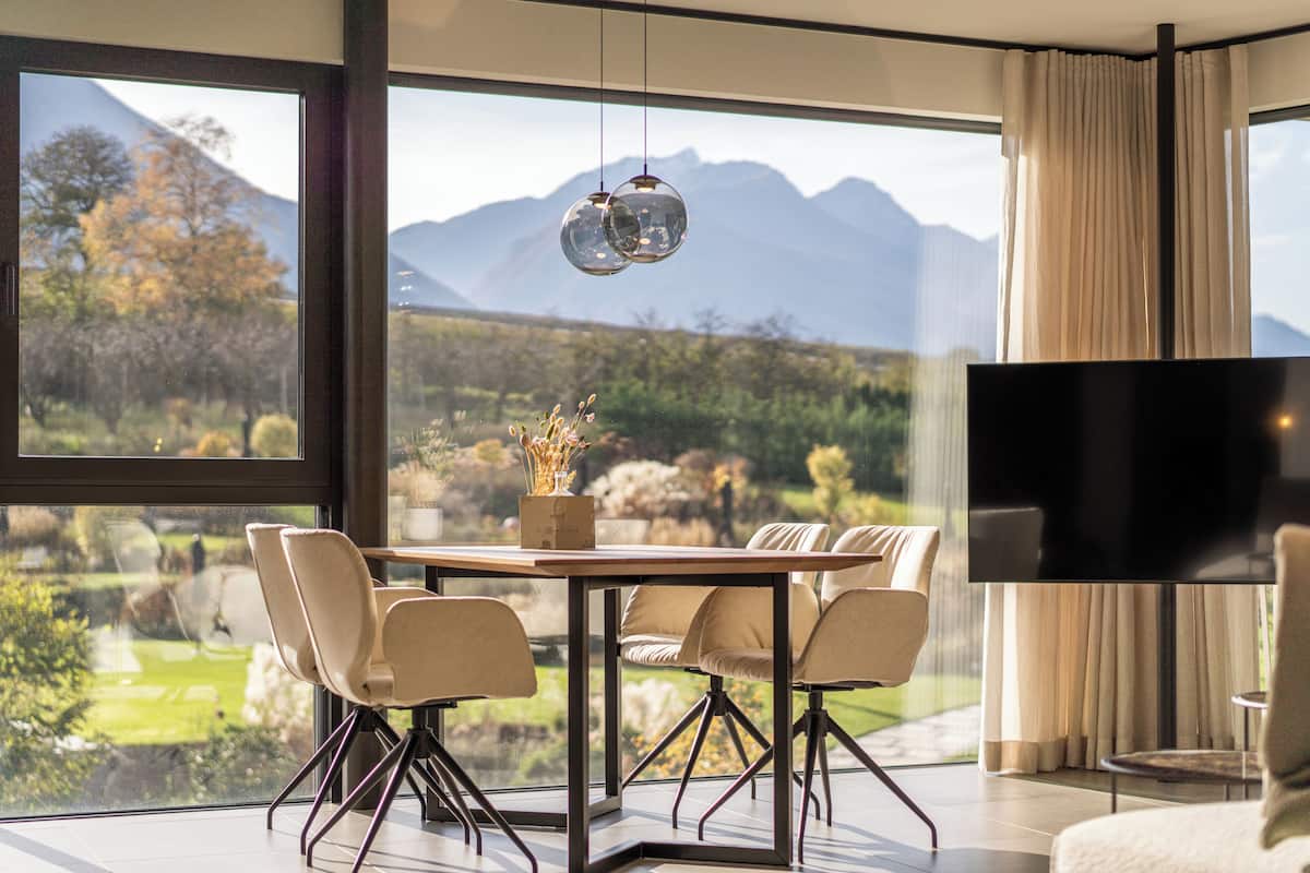 Uma área de refeições moderna com uma mesa grande e cadeiras, uma televisão de tela plana e vista para montanhas e vegetação.