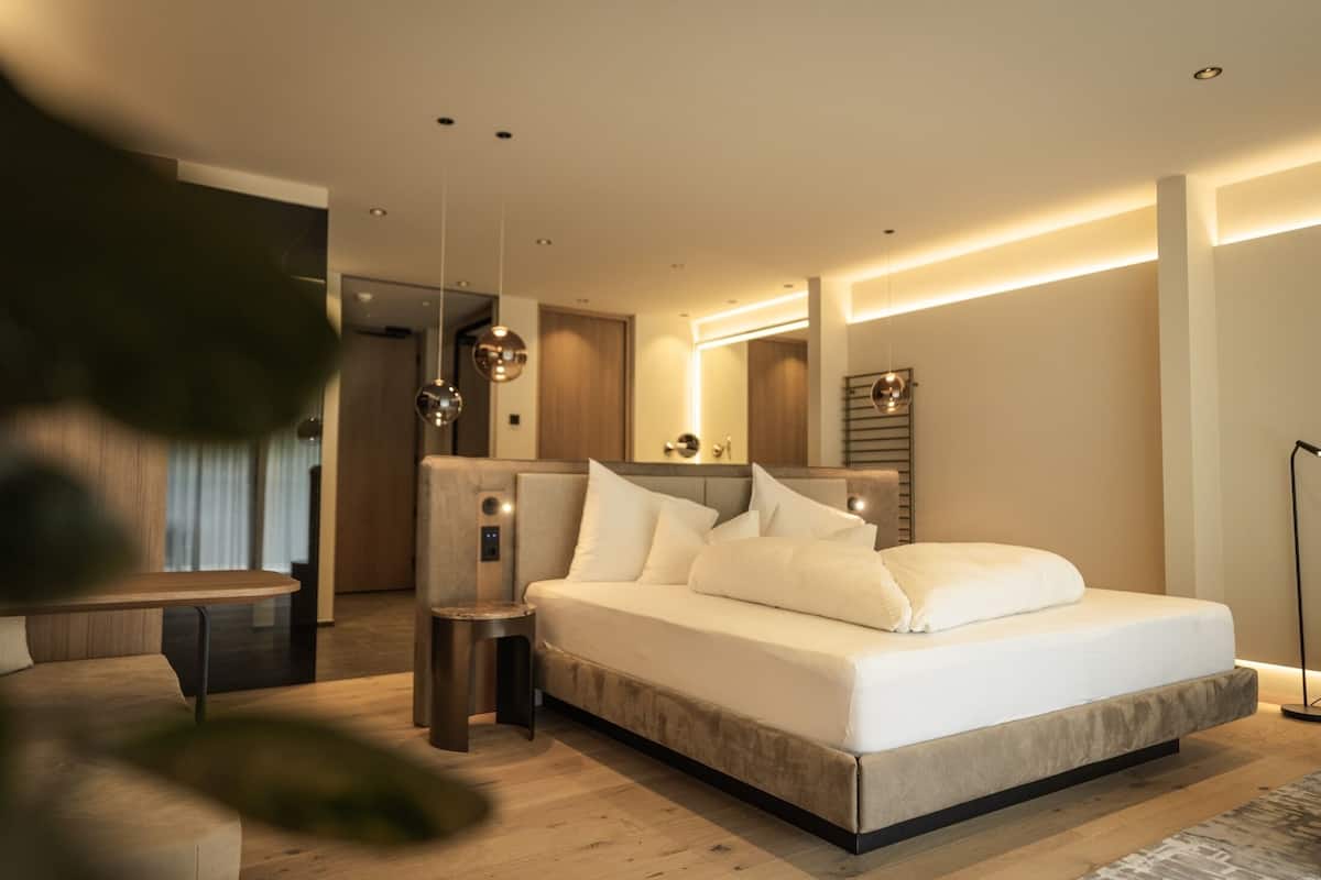 Quarto moderno com uma cama grande, mesas de cabeceira e um pequeno espaço de estar.