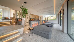 A modern living room with a large gray sofa, a small round table, and a staircase with illuminated steps. - Boutique Hotel Amaril (Castelbello-Ciardes)