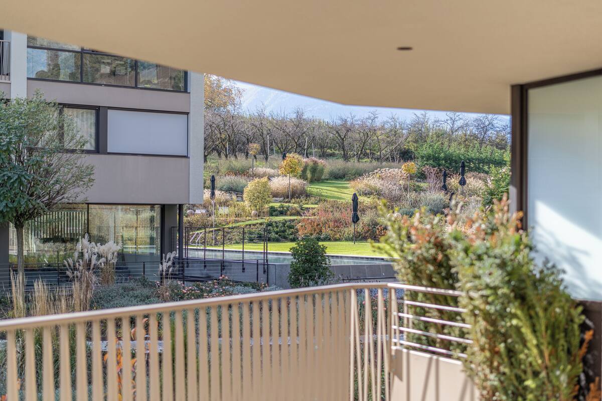 Um edifício moderno com varanda com vista para um jardim paisagístico com diversas plantas e um caminho.