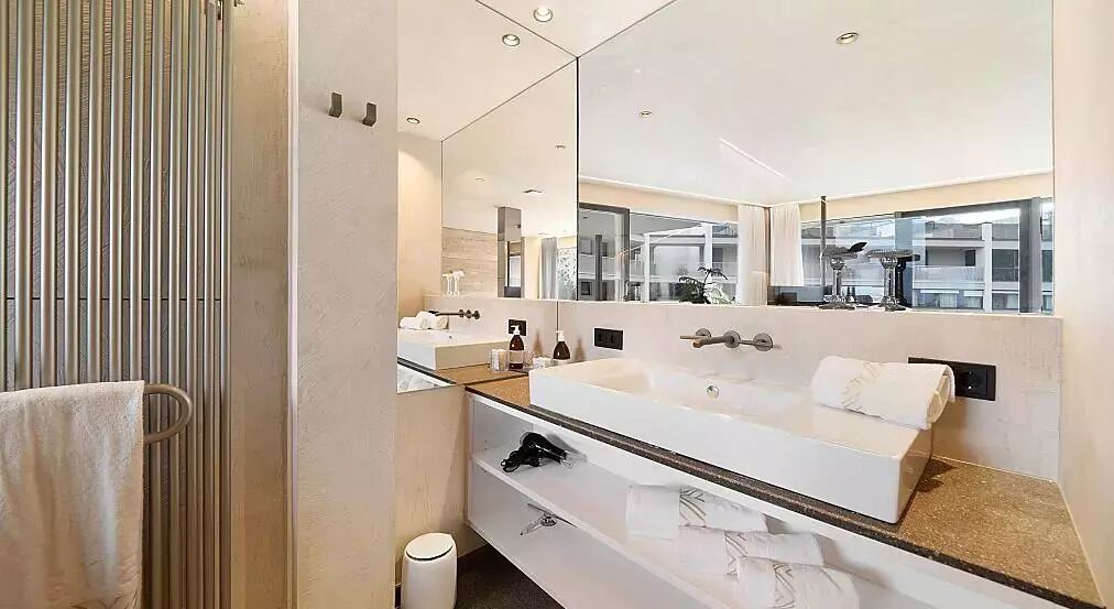 A modern bathroom with a large mirror, a white sink, and a towel rack.