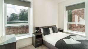 A modern bedroom with a large bed, two bedside tables, and a view of a brick building through the windows. - Spacious 3 Bed Apartment in Waterloo, Liverpool (Liverpool)