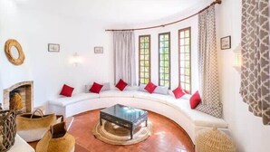 A curved white sofa with red cushions, a glass coffee table, and woven baskets. - Villa Flores - Close to the Amendoeira Golf Resort! (Pêra)