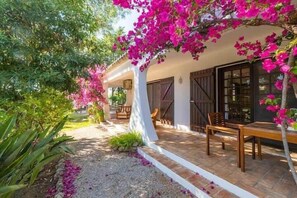 A covered outdoor seating area with a table and chairs, surrounded by lush greenery and flowering bougainvillea. - Villa Flores - Close to the Amendoeira Golf Resort! (Pêra)