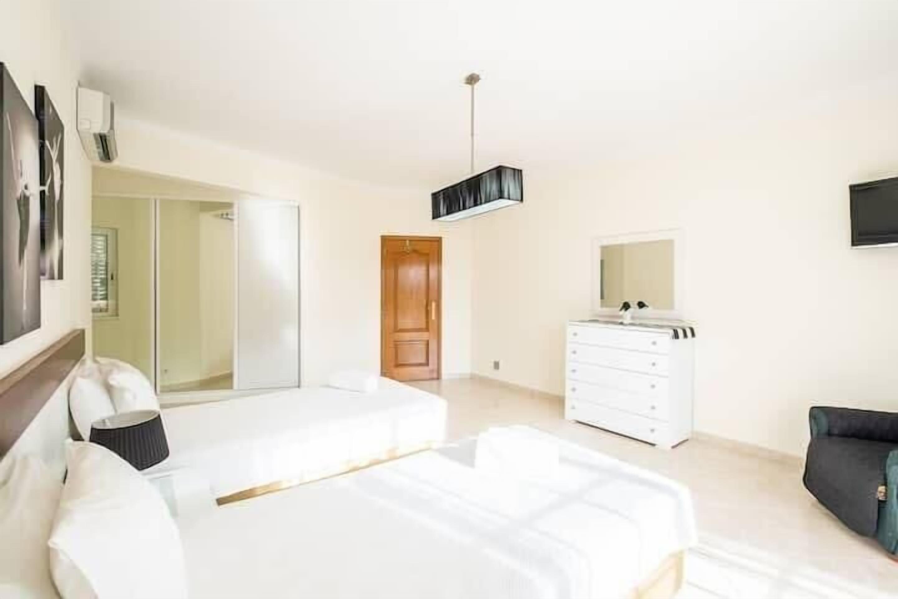 Une chambre à coucher moderne, dotée d’un grand lit, d’une commode, d’un téléviseur et d’une porte donnant accès à une salle de bain.