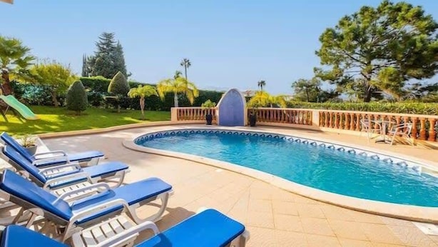 Una piscina con sillas reclinables azules y un muelle de madera.