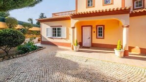Una casa de dos pisos con techo de tejas, entrada pavimentada y plantas en macetas.