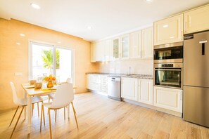 Una cocina moderna con armarios blancos, electrodomésticos de acero inoxidable y un comedor con mesa y sillas.