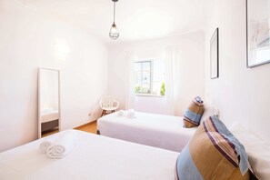 Two single beds with crisp linens, a large mirror, and a window with sheer curtains.